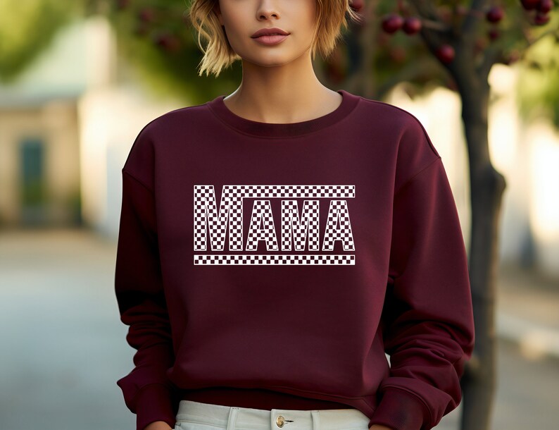 Puede incluir: Una sudadera granate con la palabra "MAMA" en letras blancas a cuadros. Las letras est&aacute;n delineadas en blanco. La sudadera tiene cuello redondo.