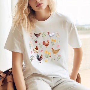 May include: White t-shirt with a colorful pattern of chickens and flowers. The chickens are brown, white, and red with yellow beaks. The flowers are pink, yellow, and blue.