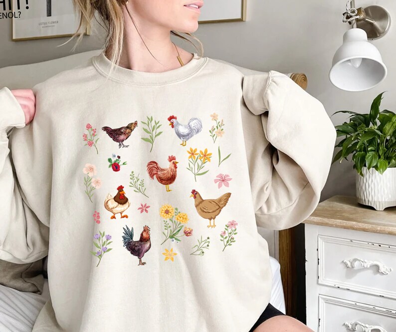 May include: A cream-colored sweatshirt with a graphic print of chickens and flowers. The chickens are brown, white, and red. The flowers are pink, yellow, and purple.