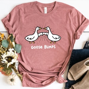 Puede incluir: Una camiseta rosa con un gr&aacute;fico de dos gansos que se miran con el texto "Goose Bumps" debajo.