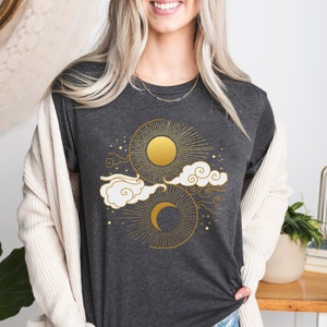 May include: A dark grey t-shirt with a gold sun and moon design. The design features a sun with rays, a crescent moon, and clouds.
