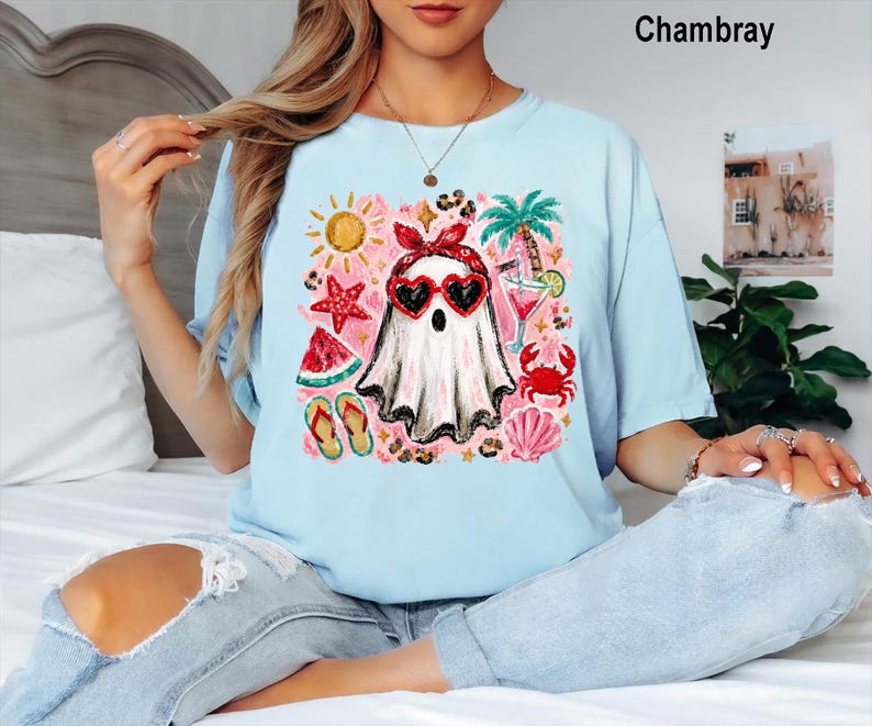 Puede incluir: Una camiseta azul claro con un estampado gr&aacute;fico de un fantasma que lleva un pa&ntilde;uelo rojo y gafas de sol en forma de coraz&oacute;n, rodeado de iconos veraniegos que incluyen un sol, una palmera, una estrella de mar, sand&iacute;a y un cangrejo.