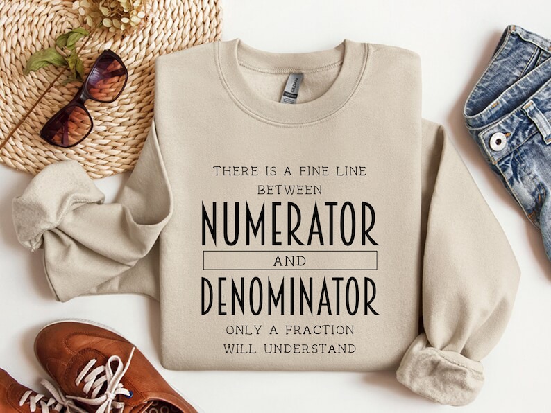 May include: A beige sweatshirt with the text "There is a fine line between numerator and denominator. Only a fraction will understand."