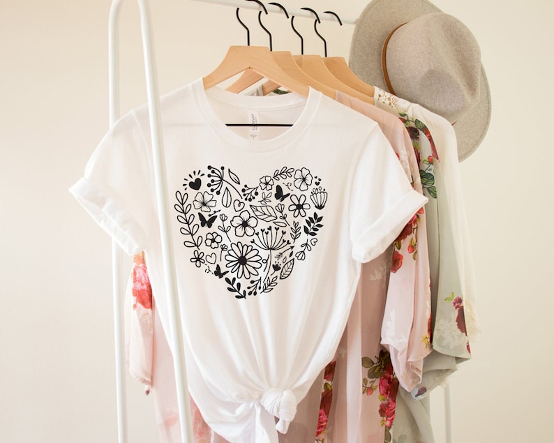 May include: White t-shirt with a black floral heart design. The heart is made up of flowers, leaves, and butterflies.