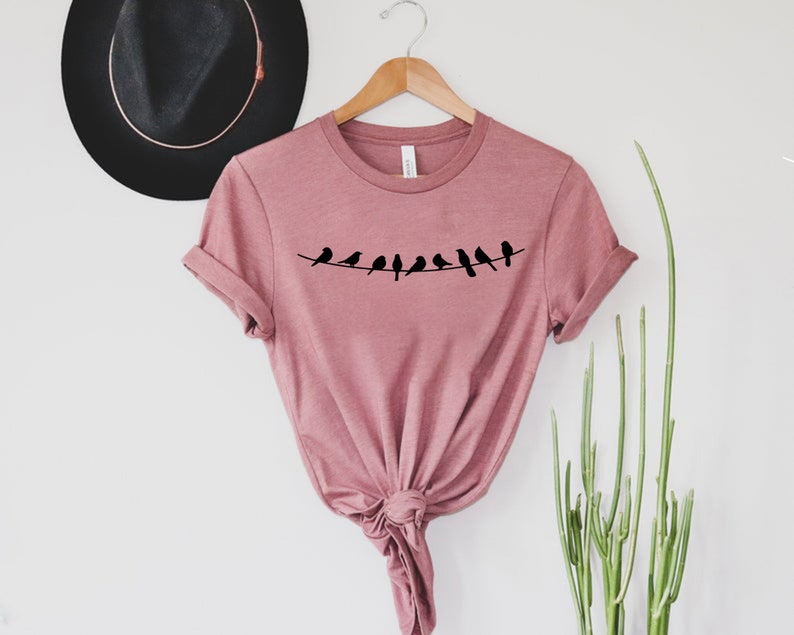 May include: A dusty rose colored t-shirt with a graphic of a line of black birds on a wire.