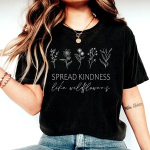 Op de afbeelding: Zwart gecropped T-shirt met een witte afbeelding van wilde bloemen en de tekst "Spread Kindness like wildflowers".