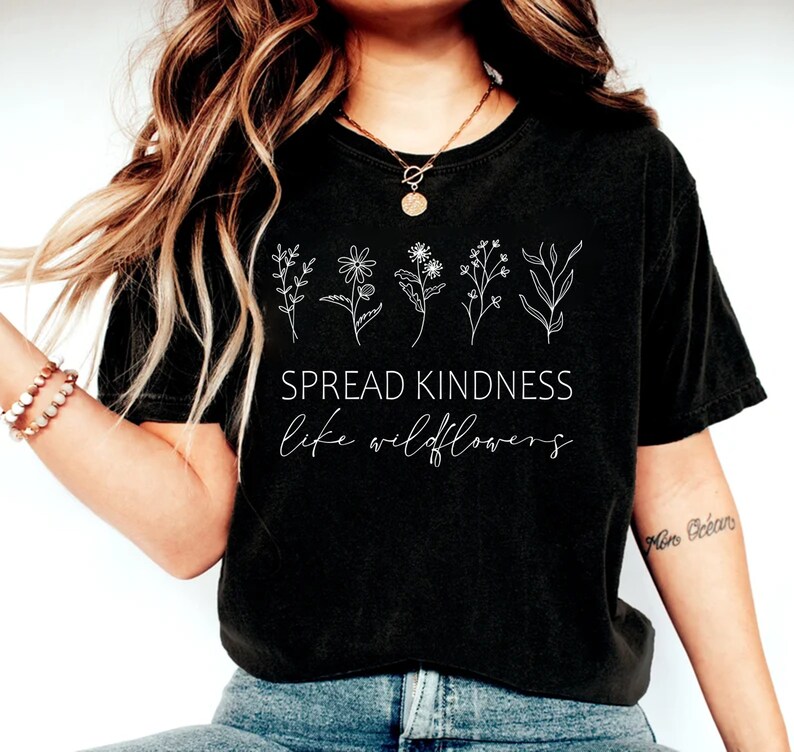 Op de afbeelding: Zwart gecropped T-shirt met een witte afbeelding van wilde bloemen en de tekst "Spread Kindness like wildflowers".