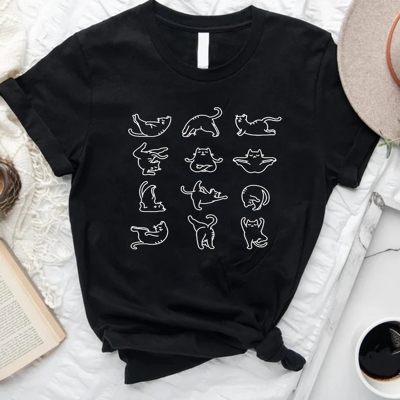 Op de afbeelding: Zwart T-shirt met een witte afbeelding van katten in verschillende yogaposes.