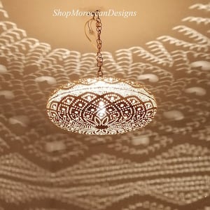 Può includere: Un lampadario marocchino rotondo di colore dorato con intricati disegni ritagliati. La luce proietta un'ombra a motivi sul soffitto.
