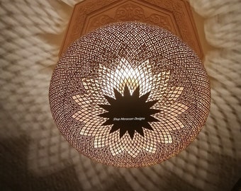 May include: A round, metal, Moroccan-style pendant light fixture with a star-shaped design in the center. The light fixture is made of a delicate, intricate latticework and casts a warm, inviting glow.