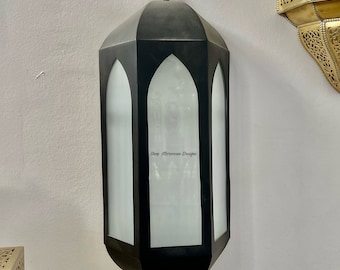 May include: Black metal Moroccan lantern with a frosted glass panel and a decorative top finial. The lantern has a rectangular shape with a pointed top and bottom.
