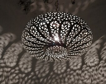 May include: A round, silver Moroccan pendant light with intricate cut-out designs. The light casts a shadow on the ceiling.