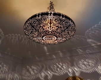 May include: A black metal ceiling light fixture with a decorative, intricate pattern. The light is on and casting a shadow on the ceiling.