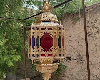 May include: A gold Moroccan lantern with intricate detailing and colorful stained glass panels. The lantern is hanging from a metal hook.