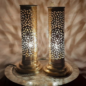 Op de afbeelding: Twee gouden metalen tafellampen met ingewikkelde uitgesneden ontwerpen. De lampen staan op een zilveren dienblad met een decoratief patroon.