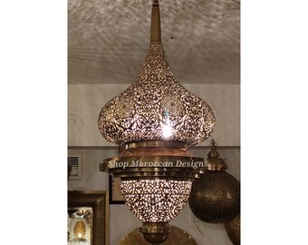 May include: A large, ornate brass pendant light with intricate cut-out designs. The light is hanging from a chain and has a round, domed shape. The light is illuminated and casting a warm glow.
