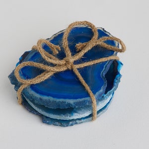 May include: Set of three blue agate coasters tied together with twine. The coasters are natural slices of agate with a blue and white pattern.