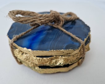 May include: Set of four blue agate coasters with gold leaf accents, tied together with twine.