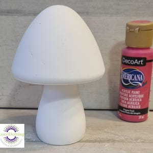 Könnte beinhalten: Eine weiße pilzförmige Keramikfigur neben einer Flasche rosa Acrylfarbe. Die Farbe ist mit "DecoArt Americana" und "Dragon Fruit" beschriftet. Die Figur ist eine leere Leinwand für Mal- und Bastelprojekte.