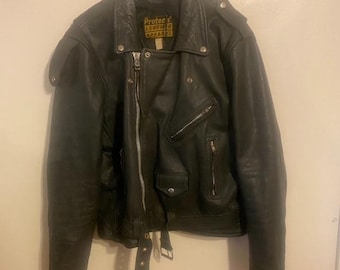 May include: Black leather motorcycle jacket with a zip fastening, multiple pockets, and a belt. The jacket has a classic biker style with a notched collar and shoulder epaulettes. The label reads "Protec Leather Apparel".