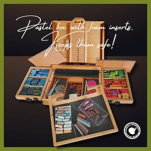 May include: A wooden box with foam inserts for storing pastels. The box is open and shows a variety of coloured pastels organised in compartments. The text "Pastel box with foam inserts. Keeps them safe!" is written on the box.