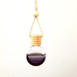 May include: A round glass car air freshener with a wooden top and a black liquid inside. The air freshener is hanging from a string.