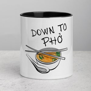 Pode incluir: Caneca de cerâmica branca com borda preta. A caneca tem uma ilustração em preto e branco de uma tigela de pho com pauzinhos e uma colher. O texto "Down to Pho" está impresso em preto na caneca.