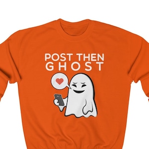 Könnte beinhalten: Orangefarbener Pullover mit einem weißen Geist, der ein Telefon und eine Sprechblase mit einem roten Herzen hält. Der Text "POST THEN GHOST" ist auf dem Pullover aufgedruckt.
