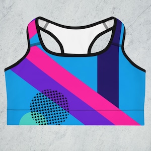 May include: A blue sports bra with a geometric pattern in pink, purple, and black. The pattern includes a large circle with a black and white design.