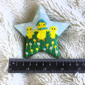 Peut inclure: Décoration en forme d'étoile cousue à la main, sur le thème du printemps. La décoration a un fond bleu clair avec un motif de ciel et de nuages. Le centre représente trois poussins jaunes dans un champ vert avec des fleurs blanches et jaunes. Mesure environ 10 cm.