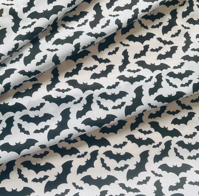 K&ouml;nnte beinhalten: Wei&szlig;er Stoff mit einem sich wiederholenden Muster aus schwarzen Fledermaus-Silhouetten. Die Flederm&auml;use sind in verschiedenen Gr&ouml;&szlig;en und in einem zuf&auml;lligen Muster angeordnet.