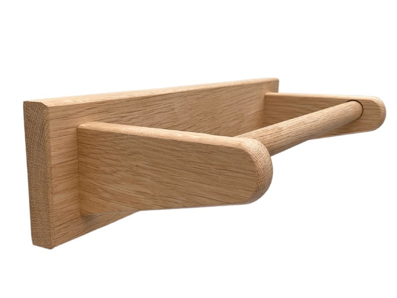 Puede incluir: Un porta rollo de papel de pared de madera con un acabado natural. El soporte tiene una base rectangular y una barra redondeada para sujetar el rollo.