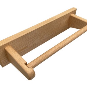 Puede incluir: Un soporte de papel de cocina de madera para montaje en pared con un acabado natural. El soporte tiene un dise&ntilde;o sencillo con una base rectangular y una varilla redonda para sujetar la toalla.