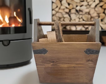 Puede incluir: Un porta leña de madera con un tinte marrón y detalles metálicos. El porta leña tiene un asa y está lleno de leña.