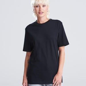 Op de afbeelding: Een zwart T-shirt met ronde hals. Het shirt met korte mouwen is gemaakt van een zacht materiaal. Het model draagt een grijze broek. De achtergrond is wit.