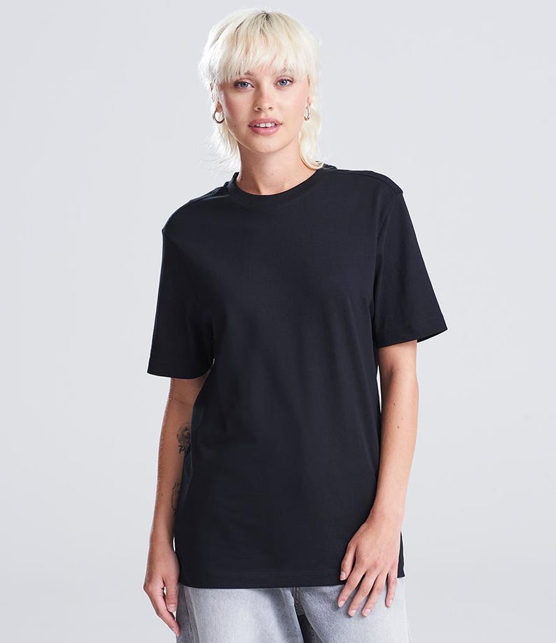 Op de afbeelding: Een zwart T-shirt met ronde hals. Het shirt met korte mouwen is gemaakt van een zacht materiaal. Het model draagt een grijze broek. De achtergrond is wit.