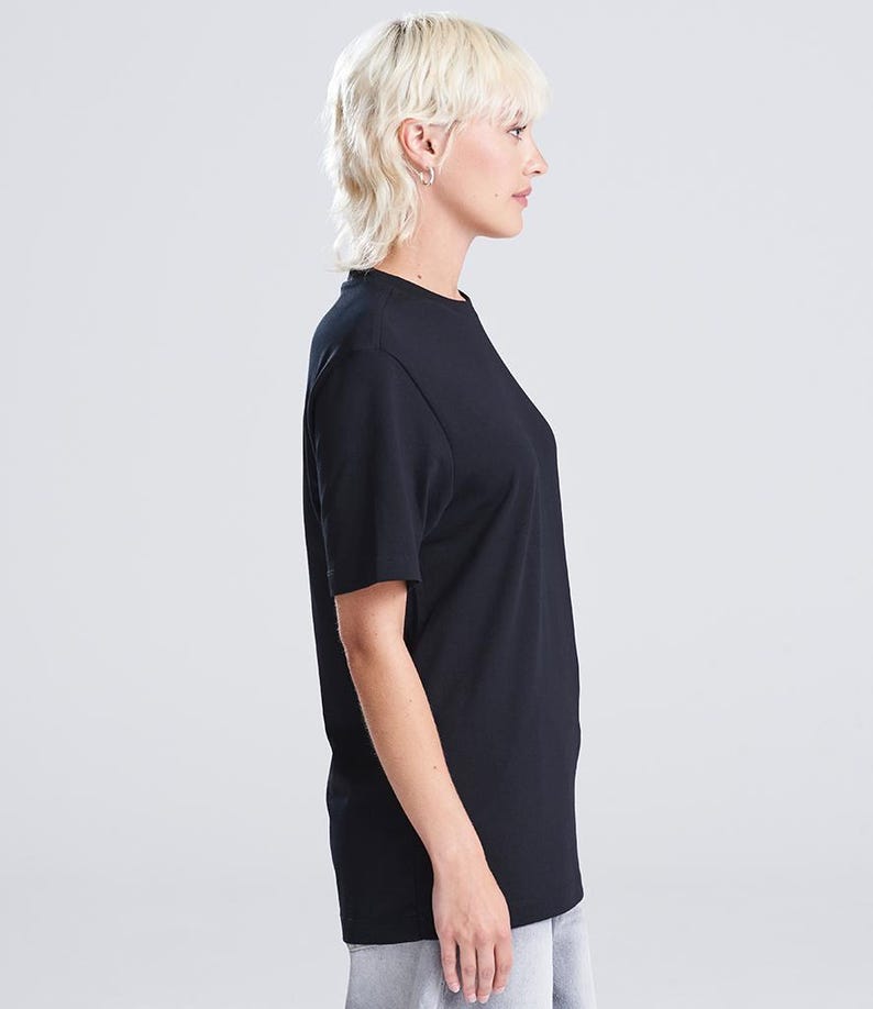Op de afbeelding: Een zijkant van een zwart T-shirt met ronde hals. De korte mouwen worden gedragen door een persoon met kort, licht haar. Het shirt lijkt gemaakt van een zacht materiaal en heeft een eenvoudig, klassiek ontwerp.
