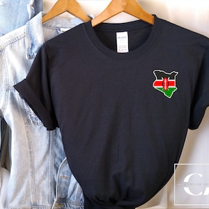 May include: Black t-shirt with a small embroidered patch of the Kenyan flag in the shape of the country. The flag is red, black, and green with a white shield in the centre.