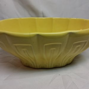 Könnte beinhalten: Eine gelbe Keramikschüssel mit gewelltem Rand und einem geometrischen Muster an den Seiten. Die Schüssel hat eine glänzende Oberfläche und wird wahrscheinlich zum Servieren oder Ausstellen verwendet.