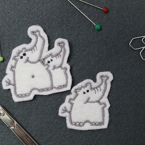 Könnte beinhalten: Drei gestickte weiße Filzpatches von Elefanten mit grauer Stickerei. Die Elefanten sind in verschiedenen Posen mit erhobenen Rüsseln.