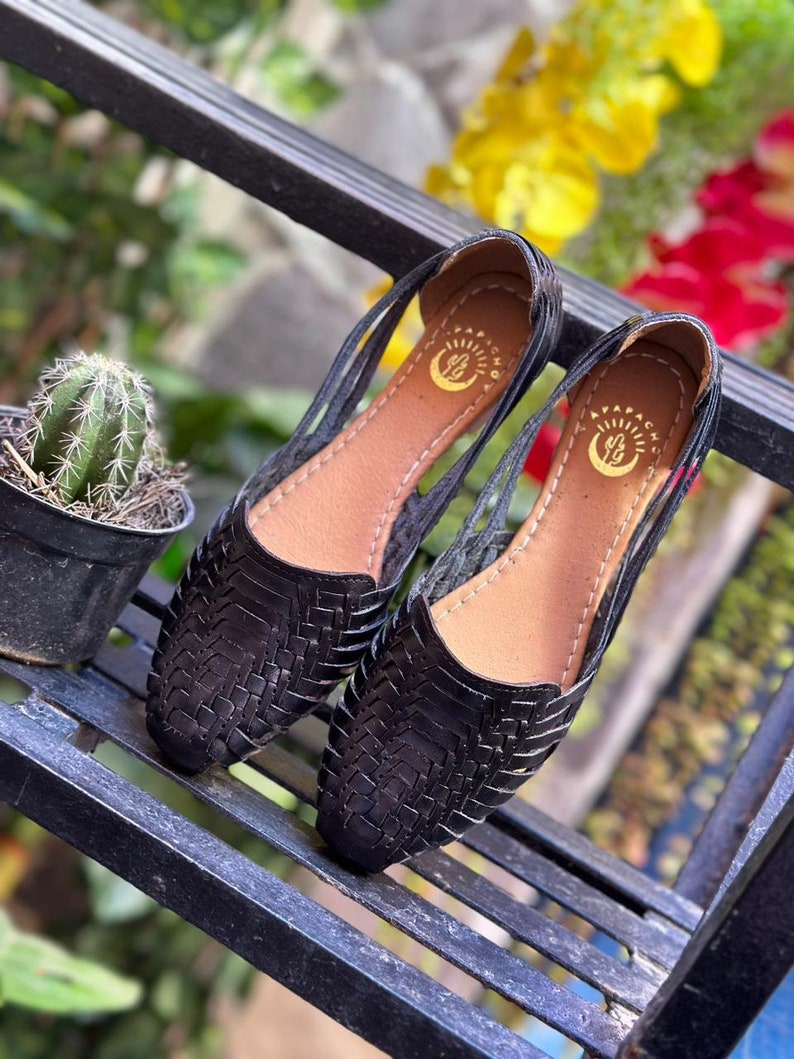 May include: A pair of black leather sandals with woven straps and a brown leather insole. The sandals have a brand logo on the insole that says "Papacayo".