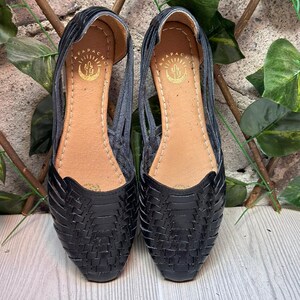 May include: A pair of black leather sandals with a woven design. The sandals have a pointed toe and a flat sole. The brand name "APACHE" is visible on the inside of each sandal.