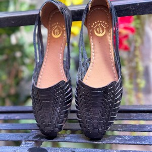 May include: A pair of black leather sandals with a woven design. The sandals have a small cactus logo on the insole.