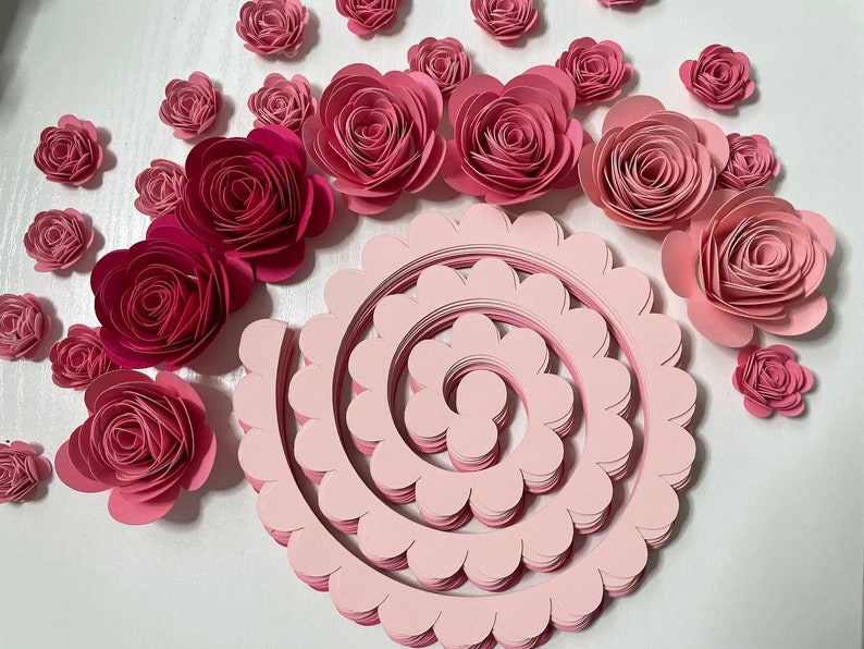 May include: A collection of pink paper flowers in various sizes, including a large spiral of pink paper petals.