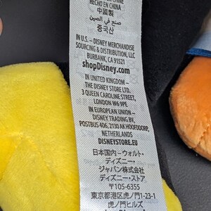 May include: A white tag with the Disney logo and text in multiple languages, including English, French, and Chinese. The tag provides sourcing and distribution information for Disney merchandise, including shopDisney.com.