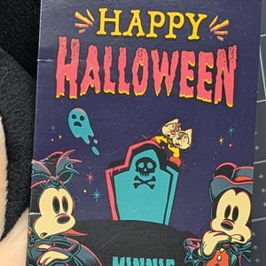 May include: A Disney Halloween-themed tag featuring Mickey and Minnie Mouse in costume. The tag reads "Happy Halloween" with images of ghosts, a tombstone, and Chip and Dale. The tag is attached to a plush toy.