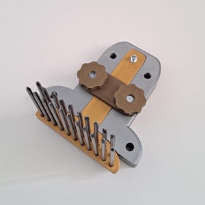 Peut inclure: Un outil imprimé en 3D gris avec une rangée d'aiguilles métalliques et deux boutons marrons. L'outil est conçu pour être utilisé avec du fil.