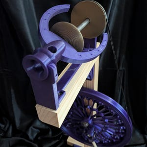 May include: A purple and wood spinning wheel with a large wheel, a smaller wheel, and a spindle. The frame is made of wood and the other parts are purple. The background is black.