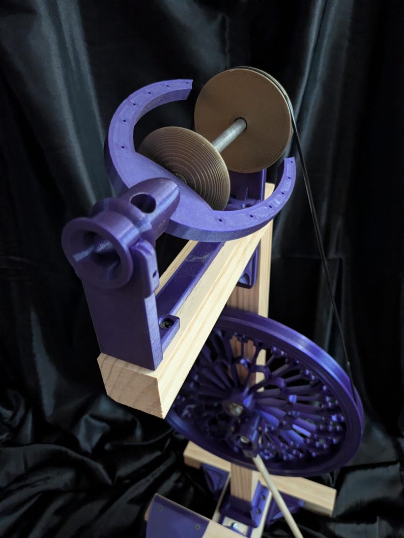 May include: A purple and wood spinning wheel with a large wheel, a smaller wheel, and a spindle. The frame is made of wood and the other parts are purple. The background is black.
