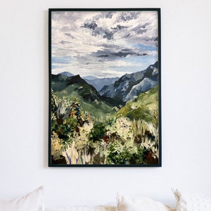 May include: A painting of a mountainous landscape with a cloudy sky. The mountains are green and the sky is a light blue with white clouds. The painting is framed in black.